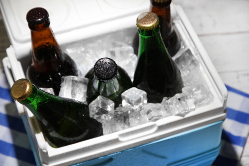 Ice chest full of drinks in bottles on color napkin, on wooden background